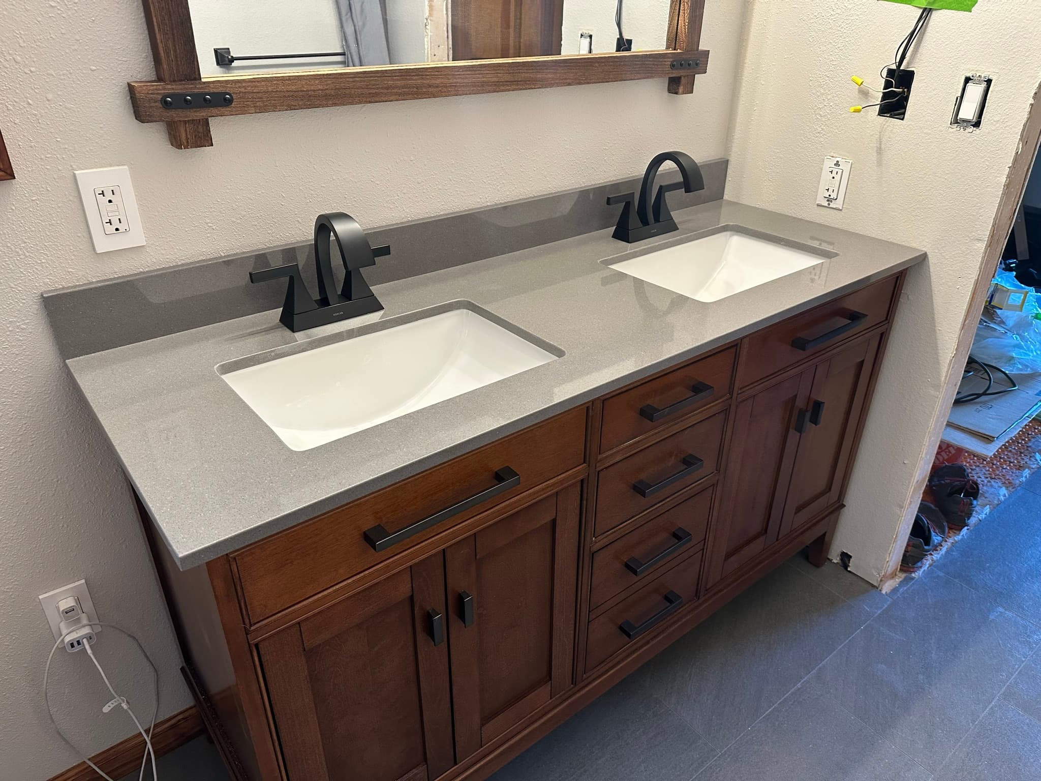 Finished double-sink vanity: Mission-style cherry cabinet, gray quartz top with two rectangular undermount sinks, matte black faucets, torched-wood mirror frame above.