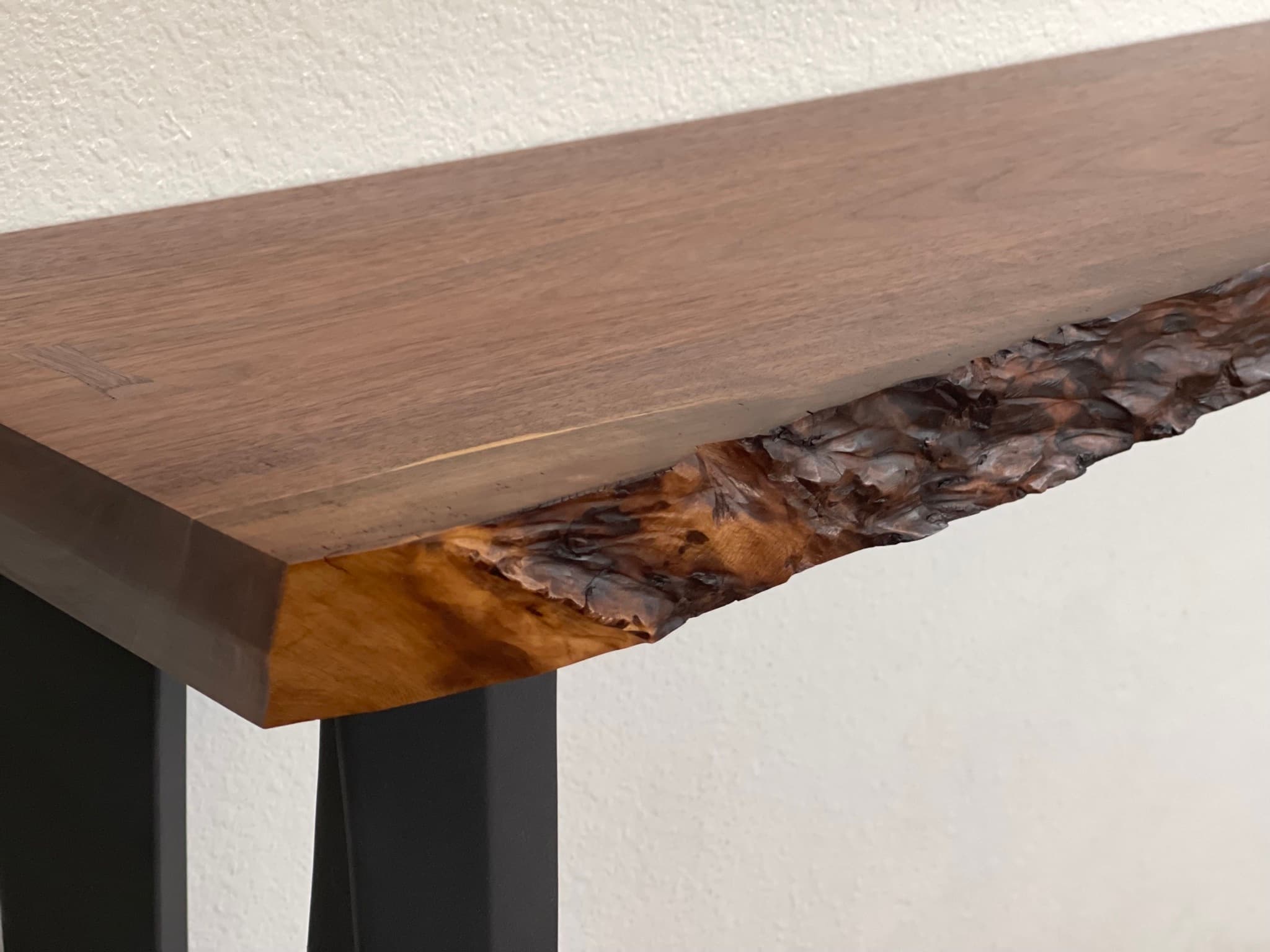 Three-quarter close-up of the console: chamfered slab end, burr live edge along the front, and one bowtie inlay visible on the top.