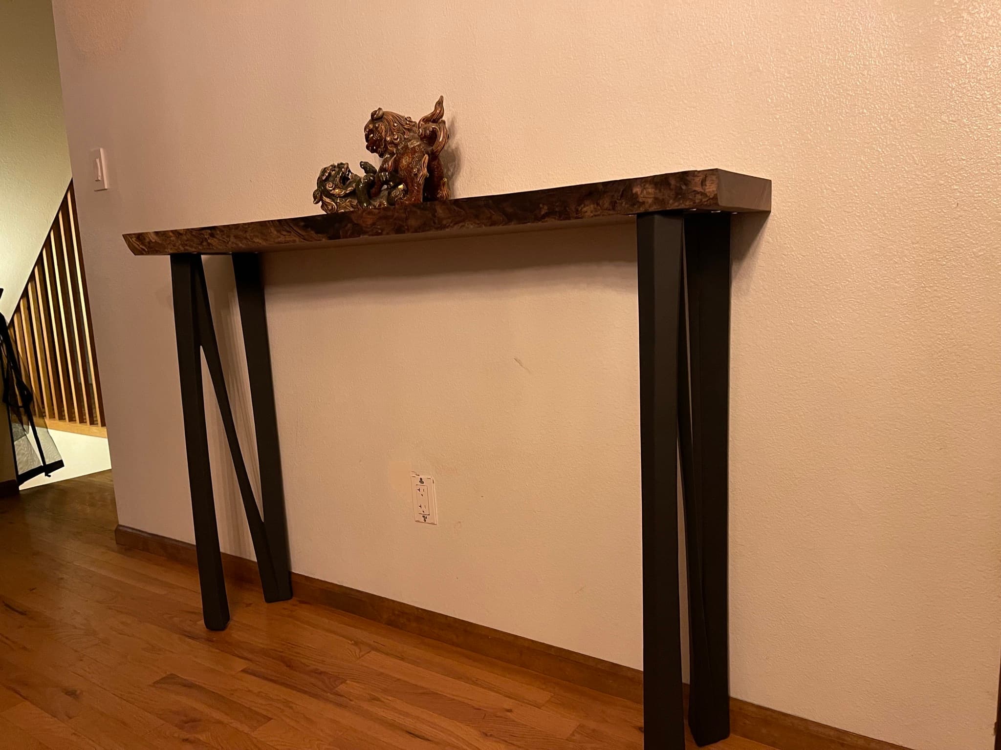 The console installed in an entry hall, styled with a bronze foo dog sculpture, the four blackened steel legs splayed wide on a hardwood floor.