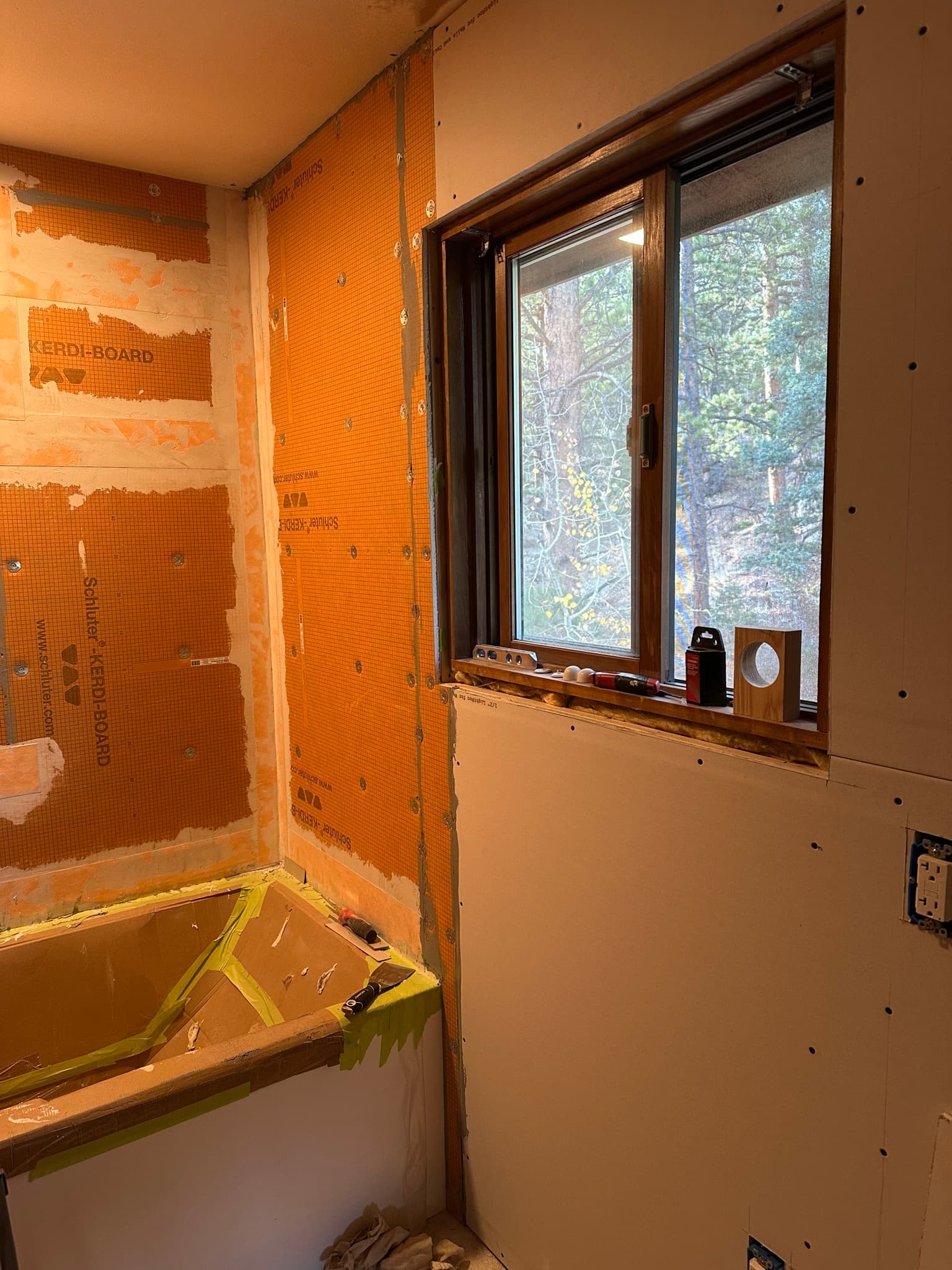 Schluter Kerdi-Band waterproofing strip applied over the seam between adjacent Kerdi-Board panels at the corner above the tub.