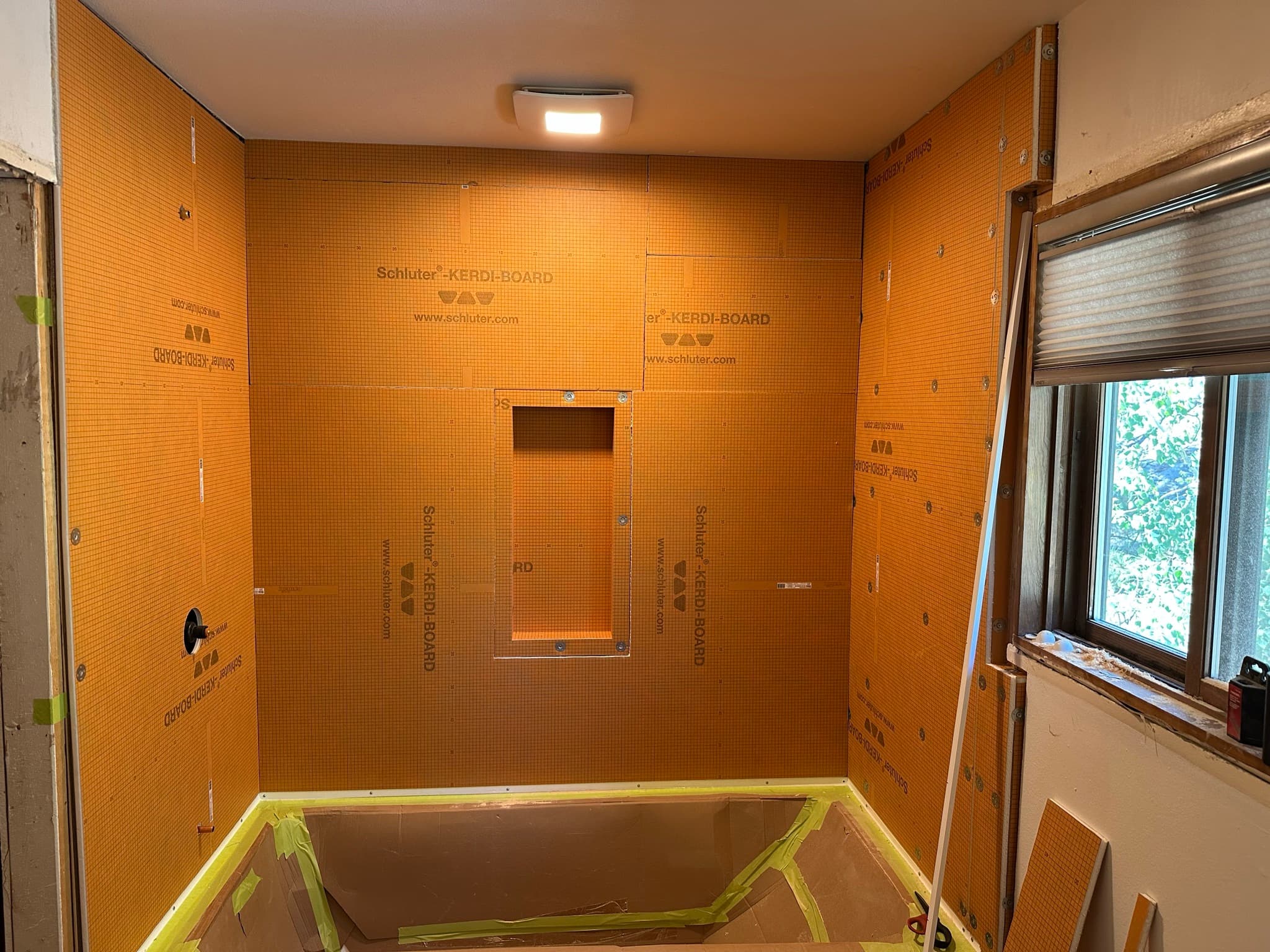 Schluter Kerdi-Board fully installed across the tub surround with cutouts for the shower valve and a recessed niche in the back wall.