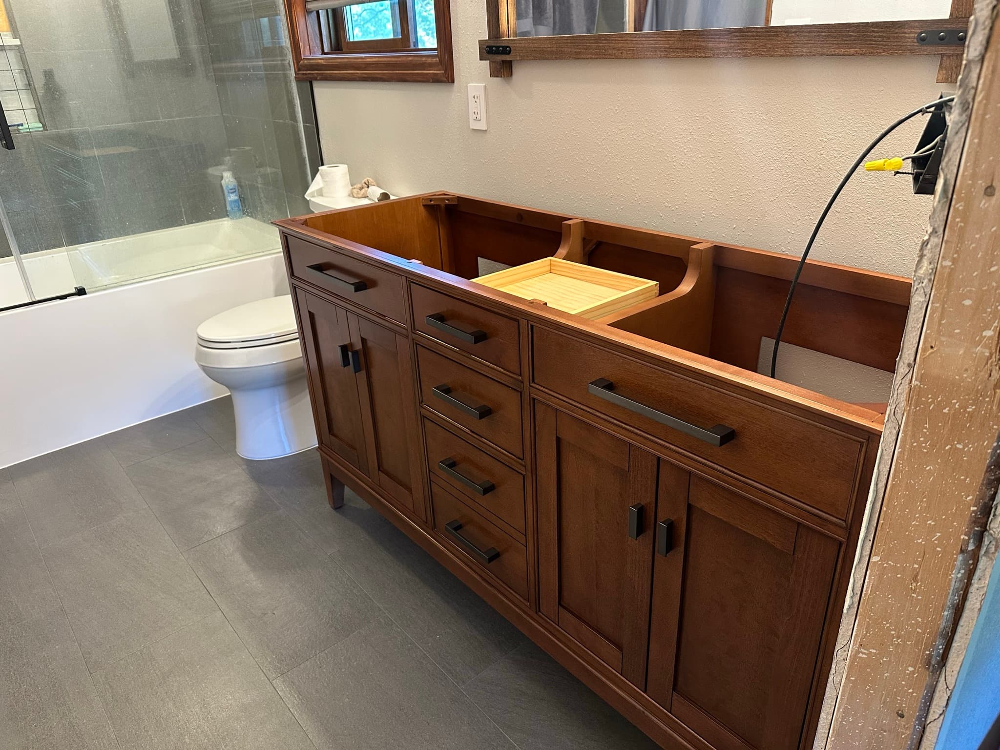 Mission-style cherry vanity cabinet installed: multiple drawers and double-door cabinets, one drawer pulled out showing dovetail joinery, top still open for the countertop.