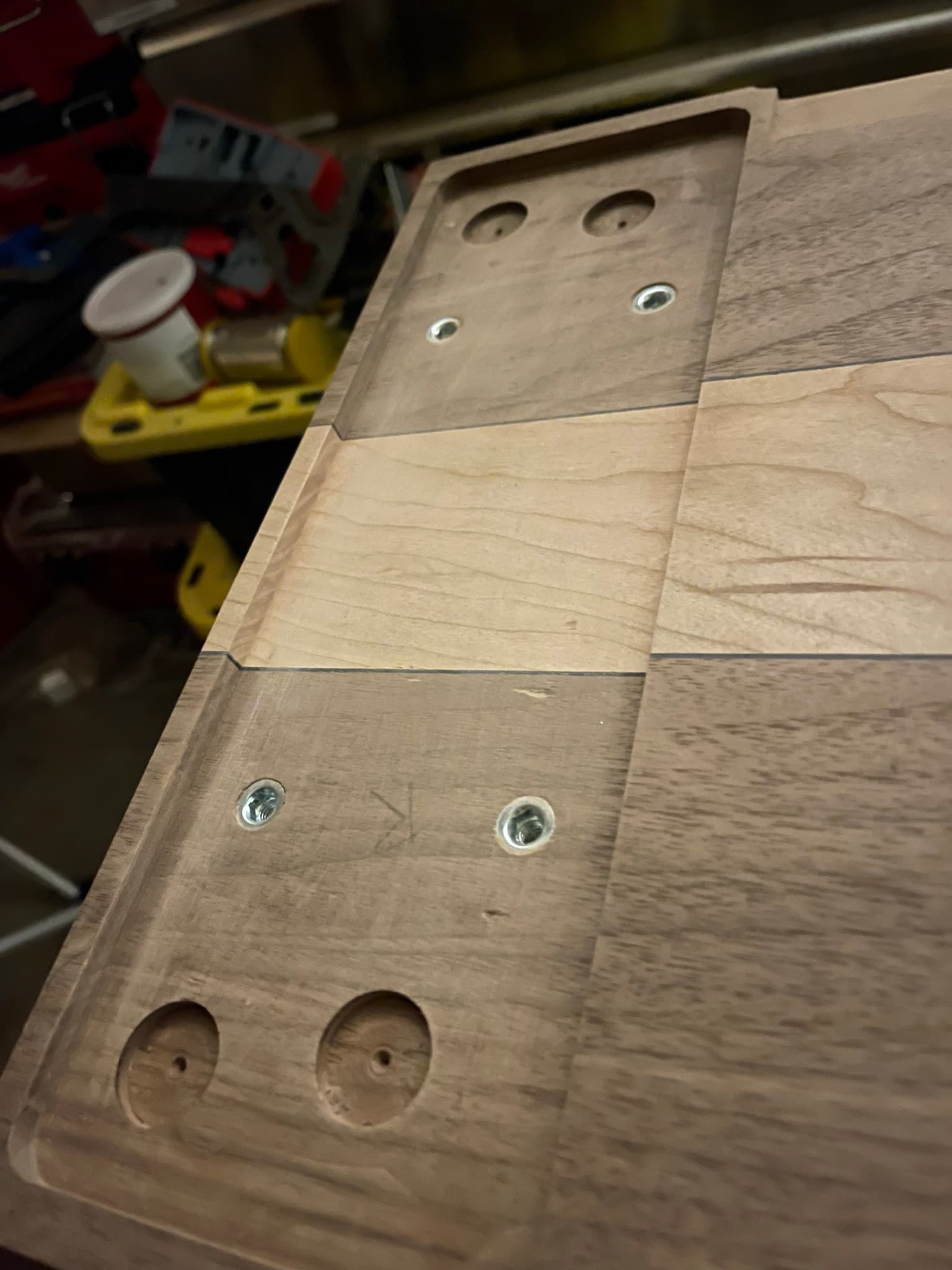 Closer view of the underside: washers and screws stepped along the maple-walnut field showing how the structural hardware is fastened into the top.
