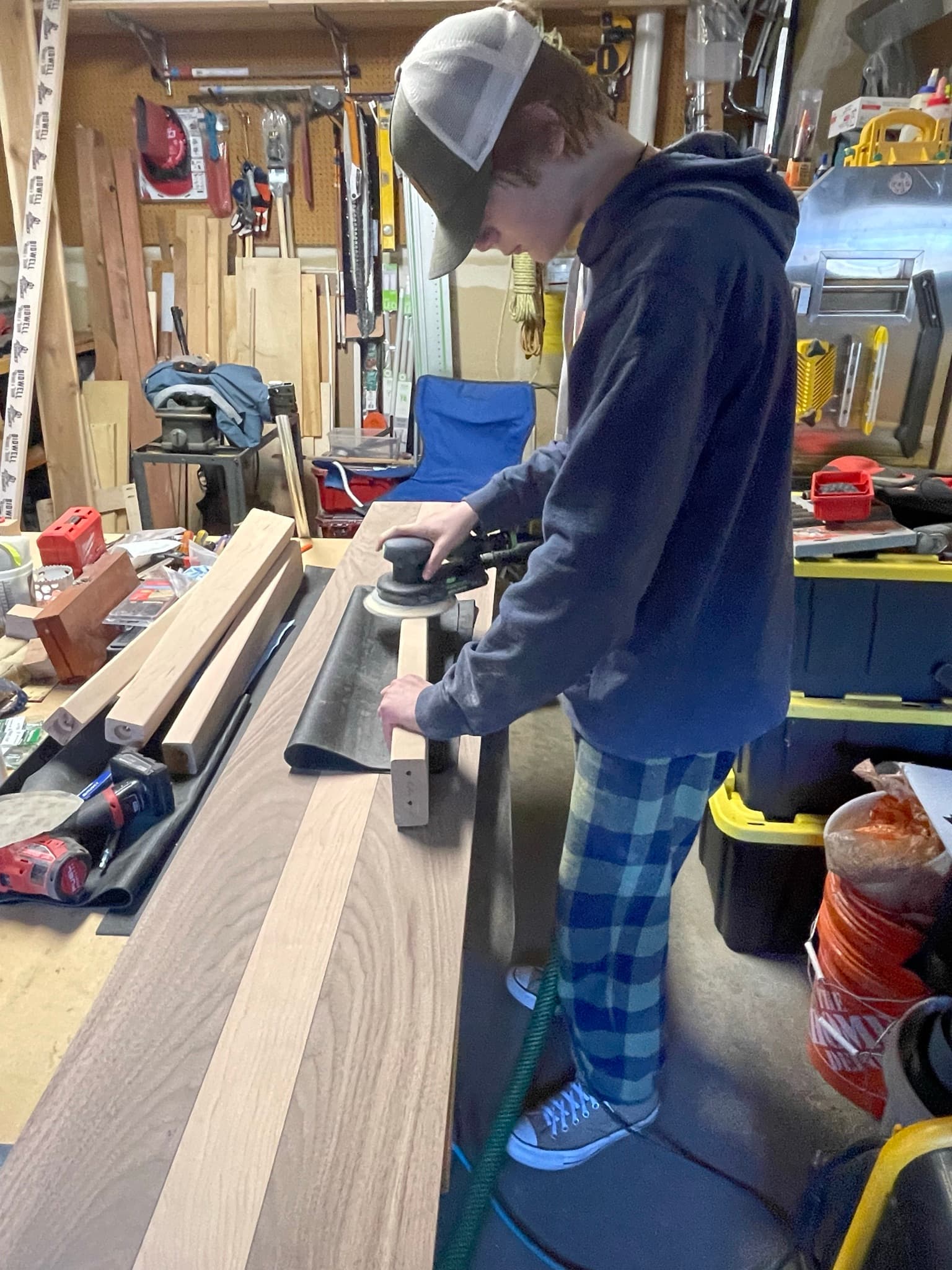 The commissioner working the top with an orbital sander in the shop, hearing protection on, sweatshirt hood up.